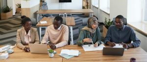 A diverse group of colleagues collaborating in a modern office setting at a wooden desk.